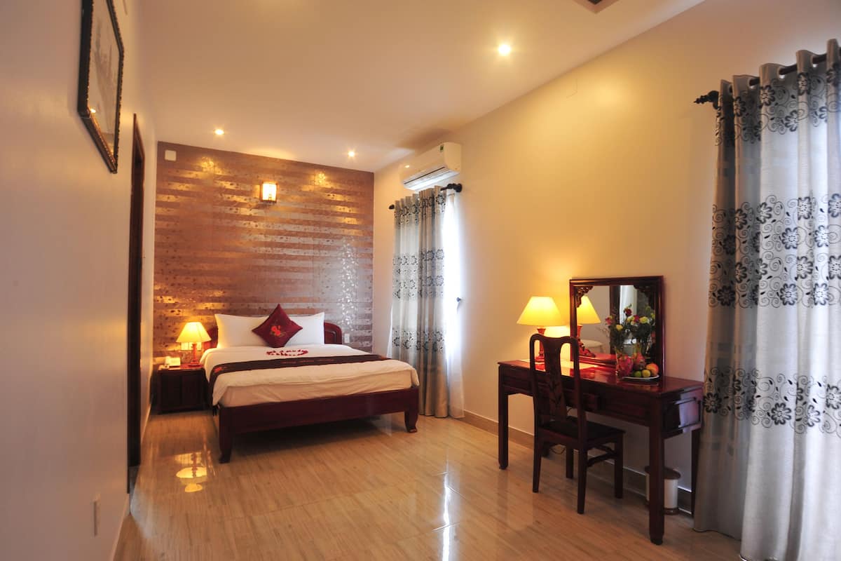 Habitación de hotel con una pared de madera decorativa, una cama con almohadas, un escritorio con lámpara y un espejo.