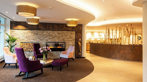 A lobby with a stone wall, a reception desk, and purple seating. - Business Class Hotel Ebersberg (Ebersberg)