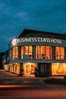 Un edificio con un letrero que dice "BUSINESS CLASS HOTEL" y varias ventanas con iluminación cálida en su interior.