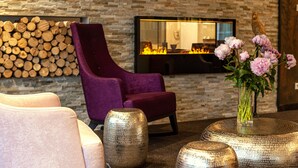 A modern lounge area with a stone wall, a fireplace, and a purple armchair. - Business Class Hotel Ebersberg (Ebersberg)
