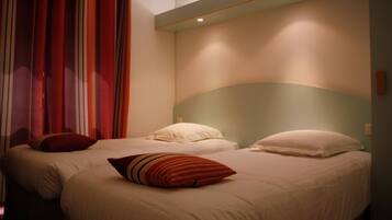 A hotel room with two beds, each with white bedding and striped pillows.