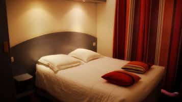 Una cama bien hecha con sábanas blancas y almohadas rojas, una mesita de noche y un cabecero.