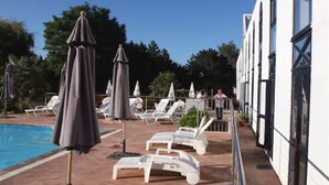 A poolside area with lounge chairs and umbrellas, a clear sky, and a building with large windows. - Agape Hotel (Bessines)