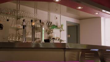 Zona de bar con estantes llenos de vasos y botellas, un mostrador con caja registradora y una puerta al fondo.