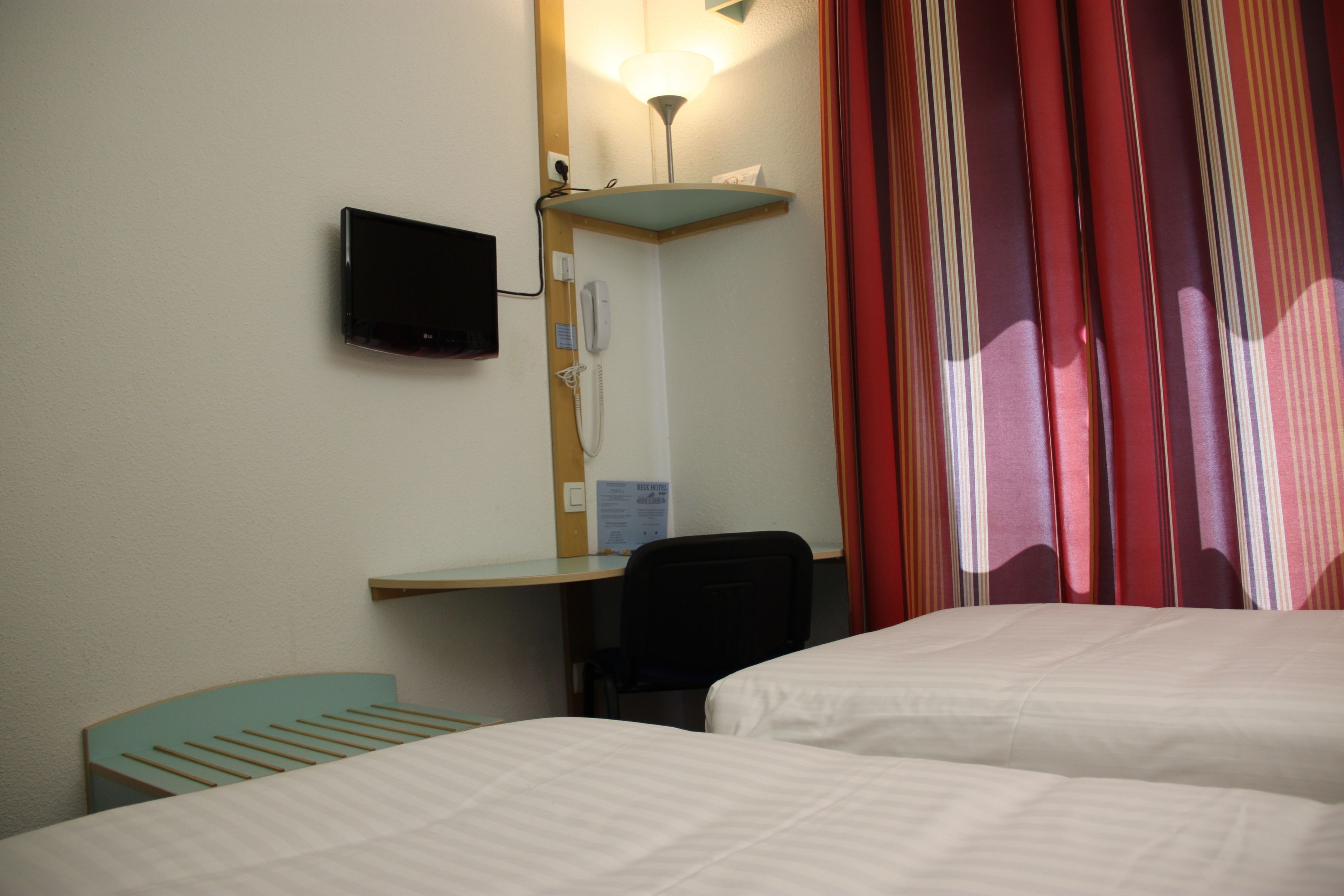 A hotel room with two beds, a desk with a chair, a flat-screen TV mounted on the wall, a telephone, and a lamp.