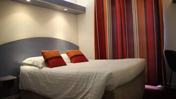A neatly made bed with white and orange pillows, a small bedside table, and a chair.
