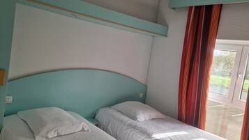 A room with two single beds, a window with curtains, and a view of the outdoors.