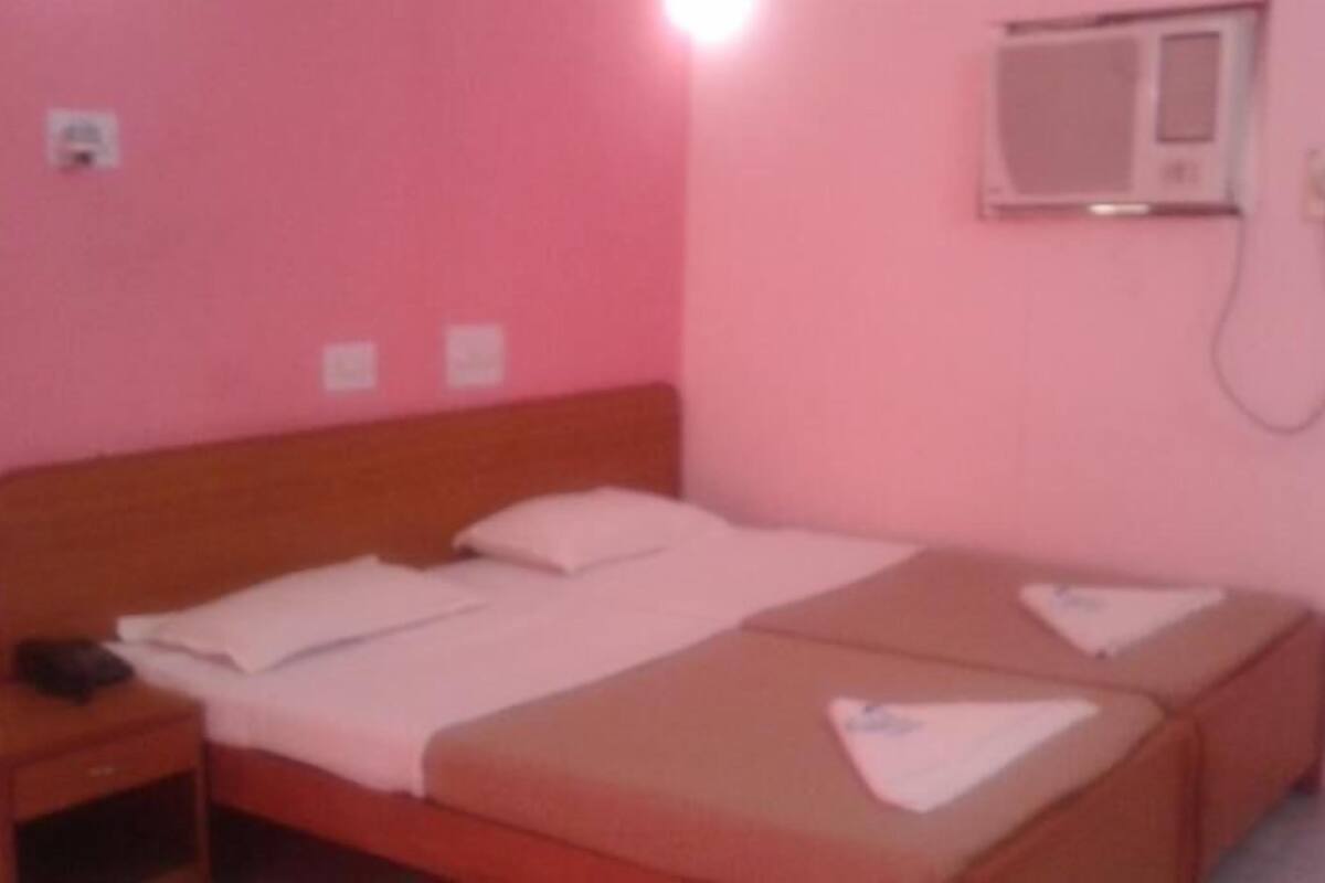 Una habitación rosa con una cama individual, una mesita de noche y un aire acondicionado de pared.