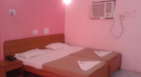 A pink room with a single bed, a bedside table, and a wall-mounted air conditioning unit.