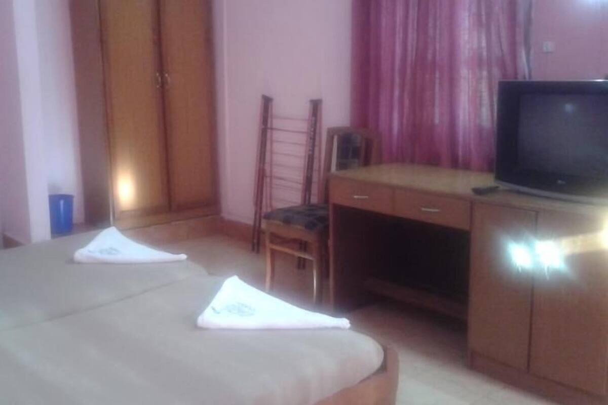 Una habitación de hotel con cama, escritorio, silla, televisor y armario.