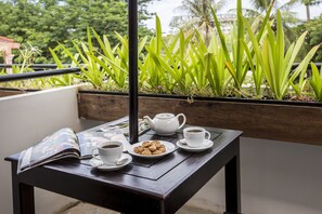 A table with a teapot, cups, and cookies on a balcony with plants in the background. - G&Z Urban Hotel (Siem Reap)
