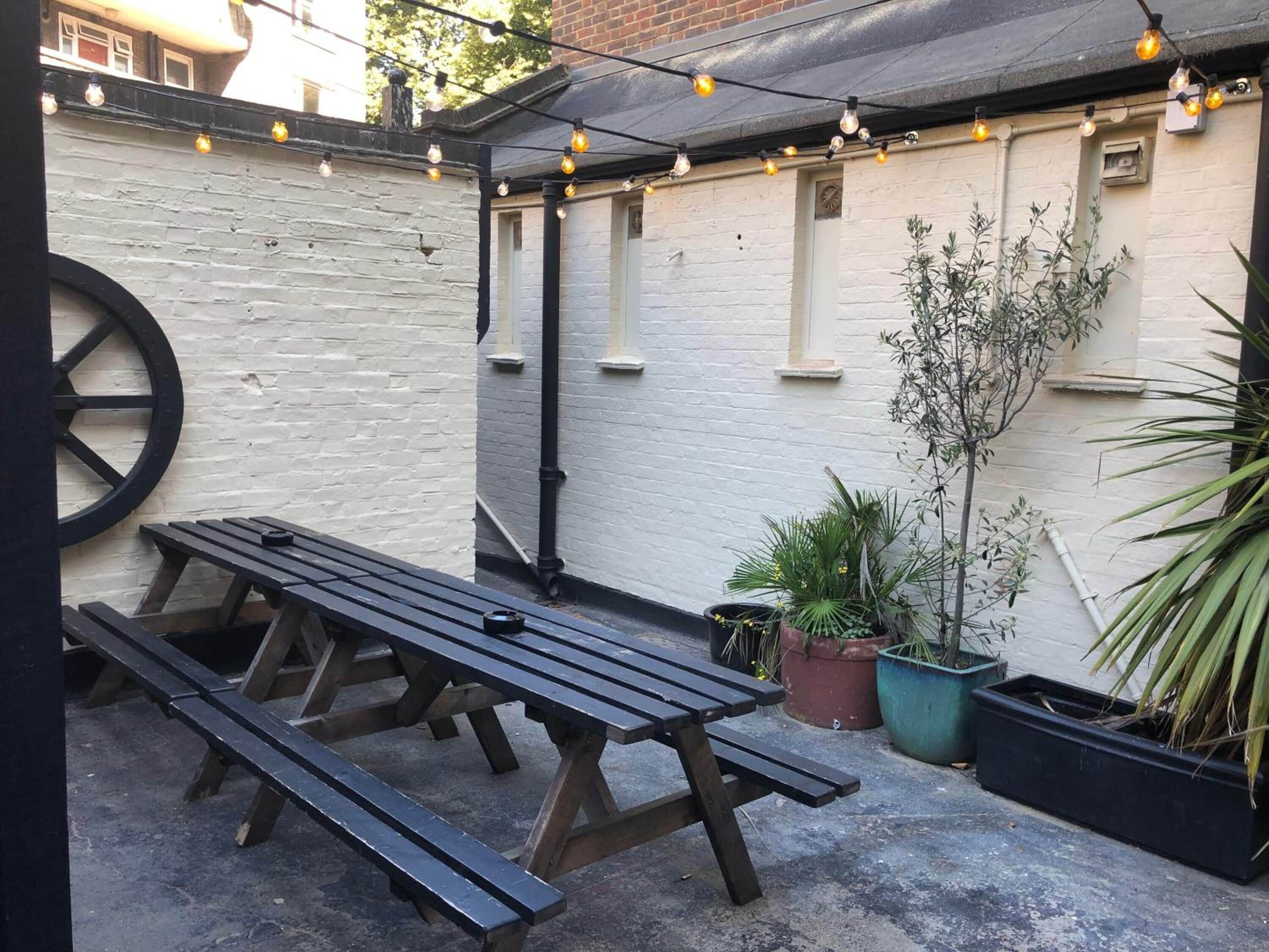 A patio area with a wooden table and benches, string lights, and potted plants.