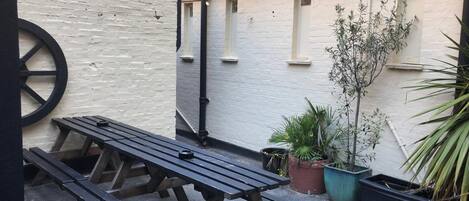 A patio area with a wooden table and benches, string lights, and potted plants.