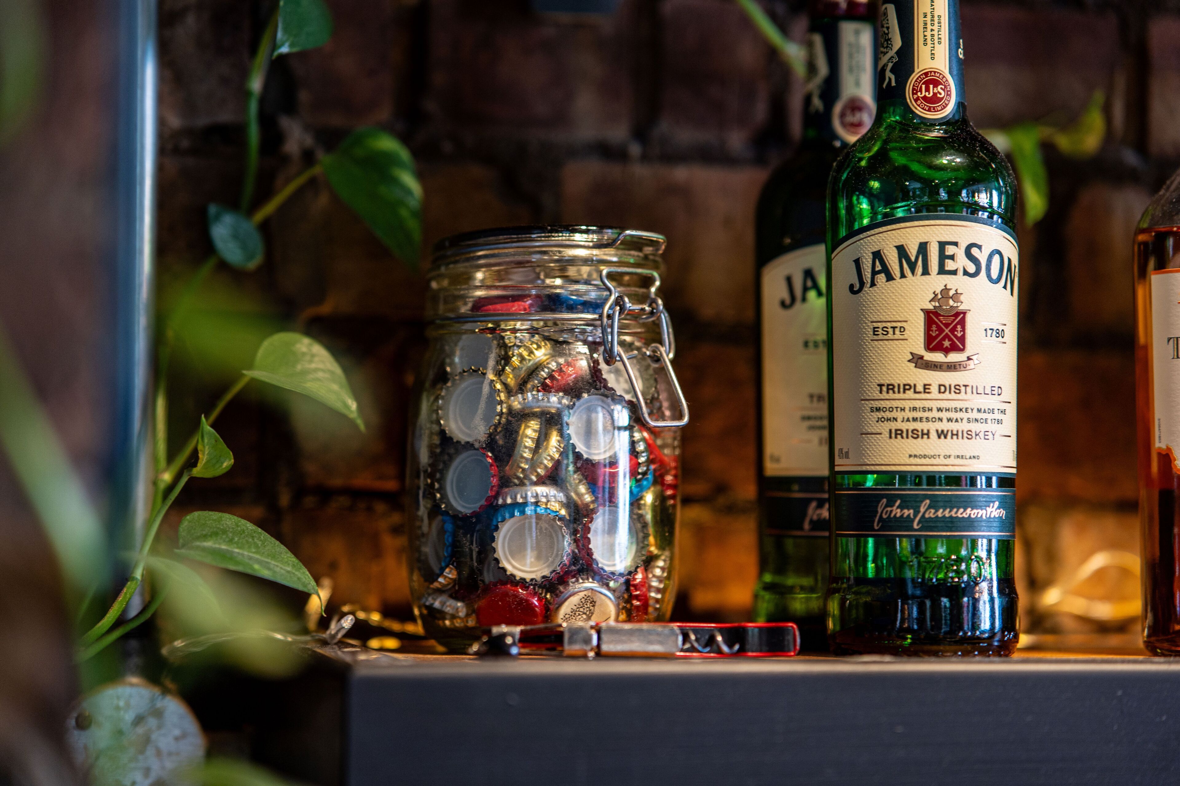 Une bouteille de whisky irlandais Jameson et un bocal rempli de différents bouchons de bouteille.