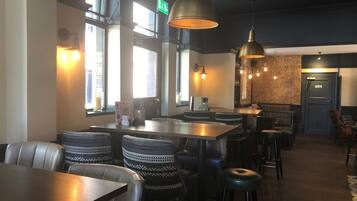 A restaurant interior with high tables, leather booths, hanging pendant lights, and brick walls.