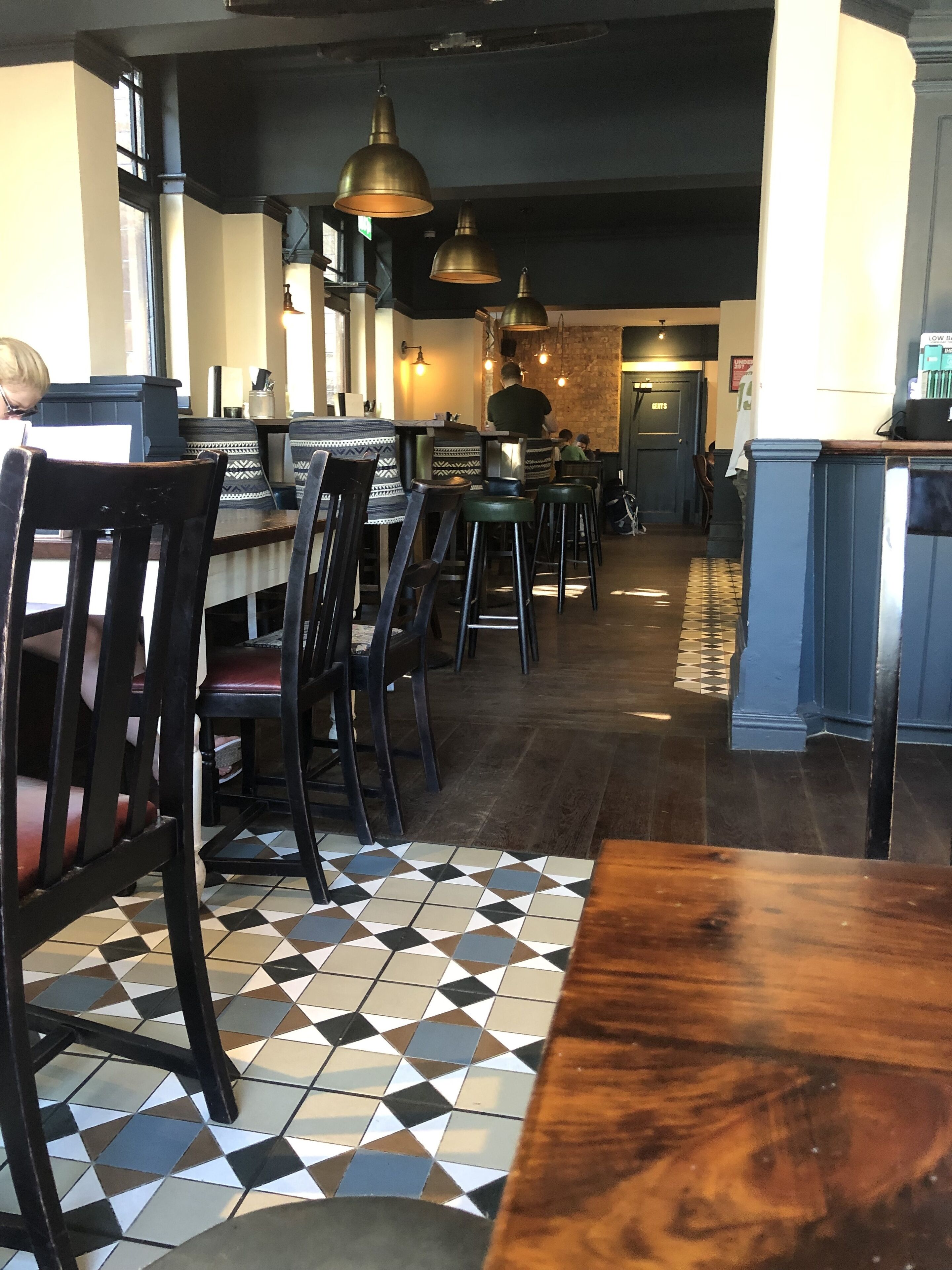 A restaurant interior with a checkered floor, wooden tables, and black chairs.
