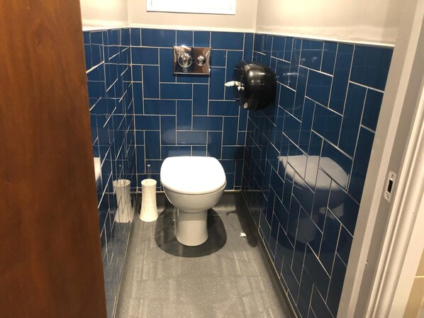 A small bathroom with a white toilet, a black trash bin, and a blue tiled wall. - PubLove @ The Steam Engine - Hostel (London)