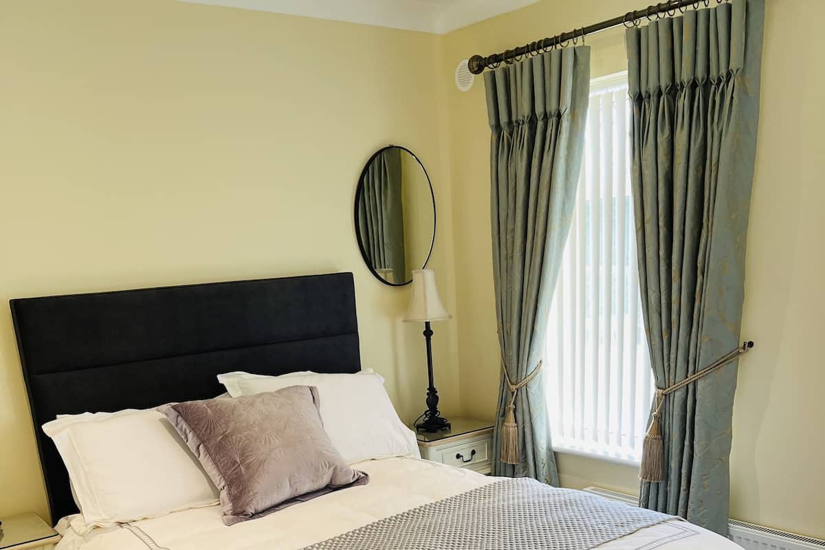 A neatly made bed with white and grey bedding, a black headboard, and a bedside table with a lamp.