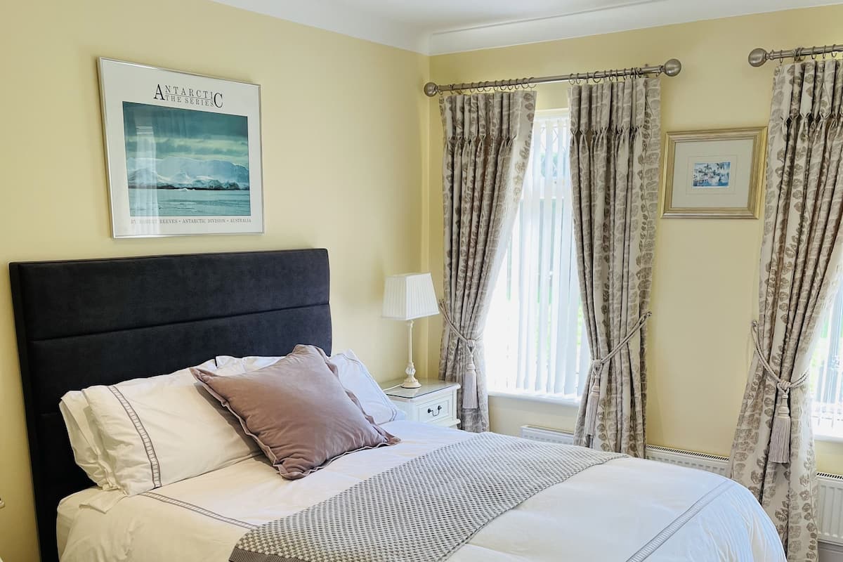 A neatly made bed with a headboard, a bedside table with a lamp, and curtains on the window.