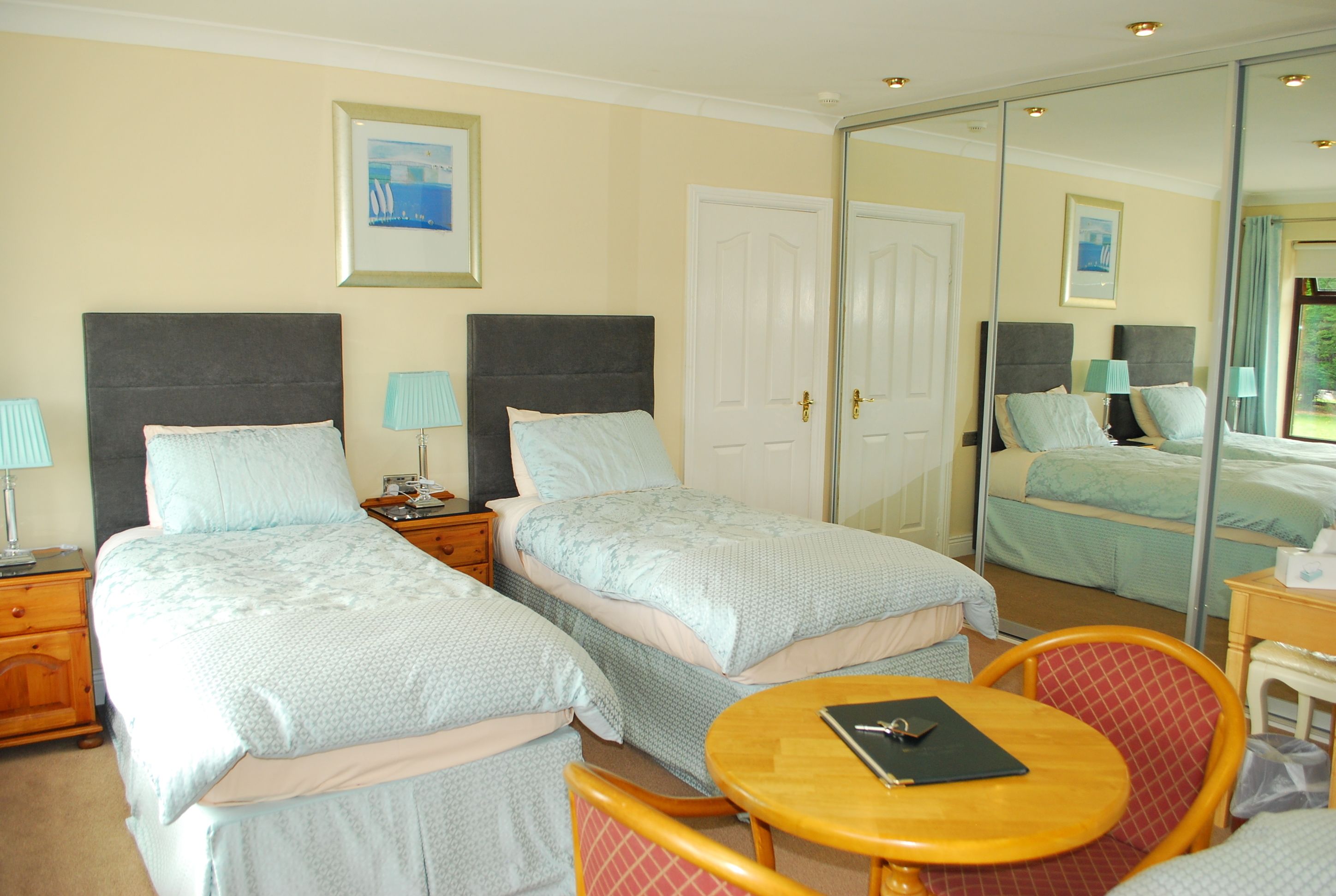 A hotel room with two beds, a round table, and a mirror.
