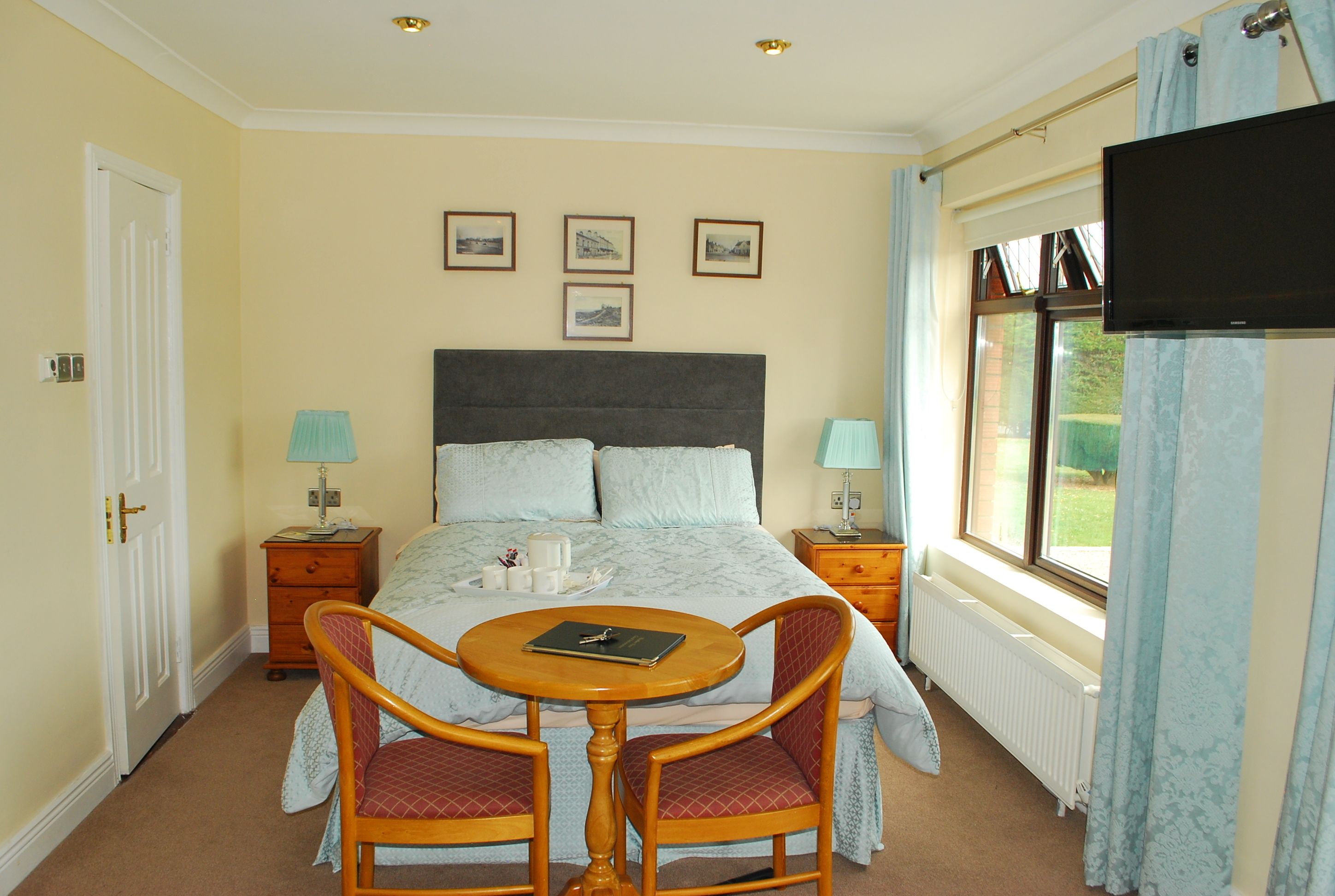 Une chambre d’hôtel avec un lit, deux tables de chevet, une télévision et une petite table avec des chaises.