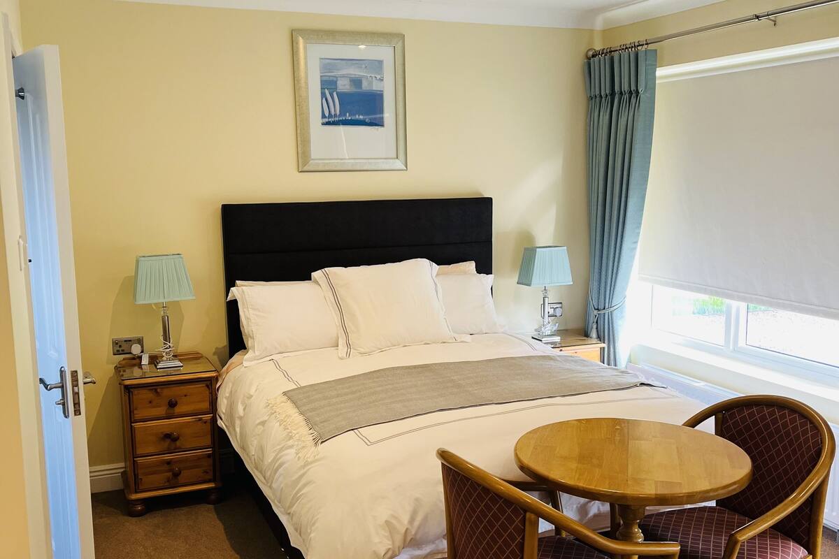 A hotel room with a bed, bedside table, lamp, chair, and a view of the outdoors.