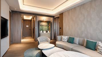 A modern hotel room with a sofa, a coffee table, a TV, and a bathroom with a shower and toilet.