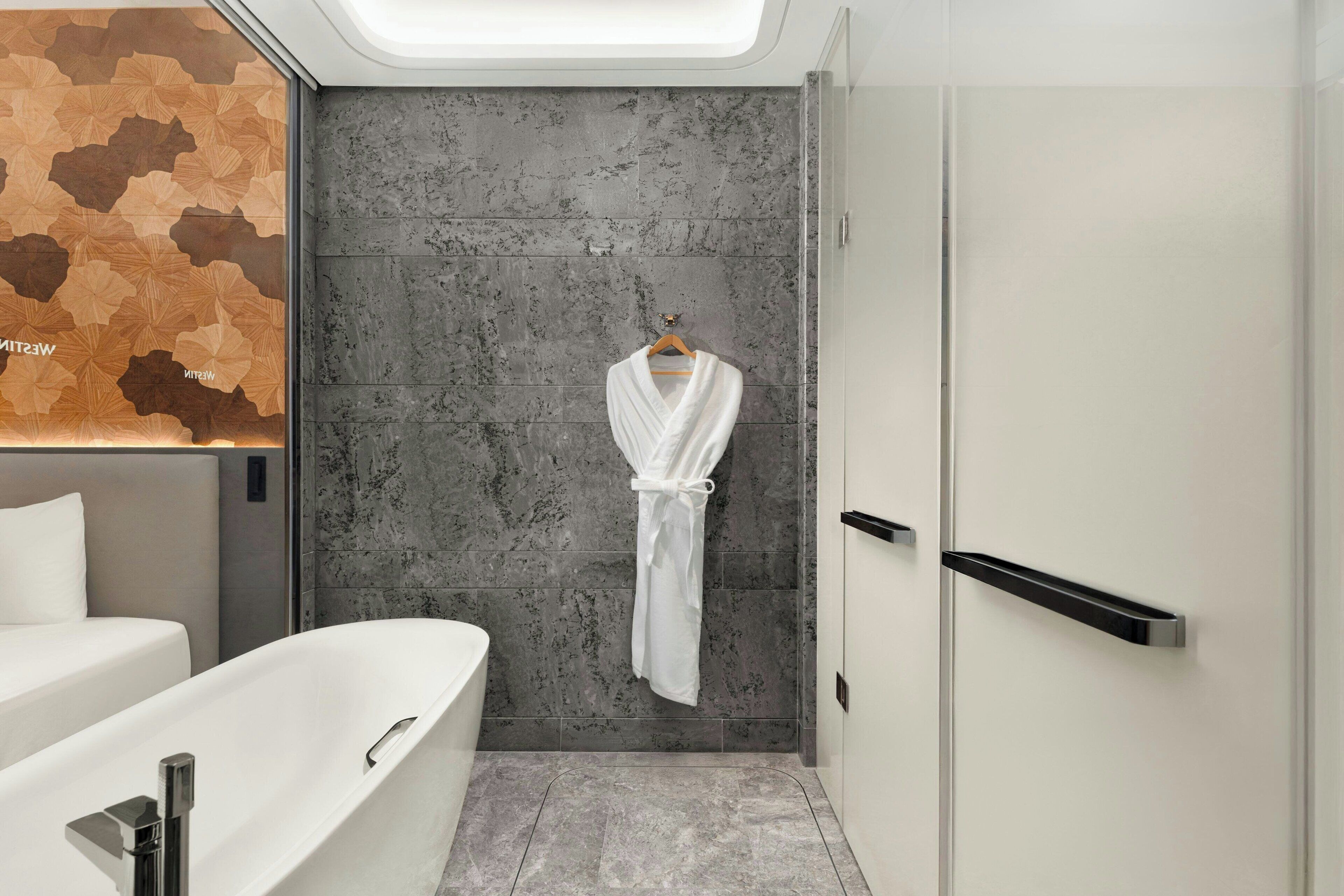 A modern bathroom with a bathtub, a towel rack with a white towel, and a textured wall.