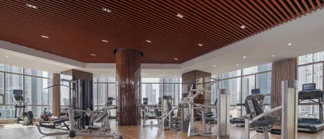 A spacious gym with various exercise equipment, large windows, and a wooden ceiling.