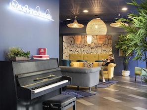 Um lobby moderno com um piano de cauda, assentos confortáveis, parede estampada e iluminação ambiente.