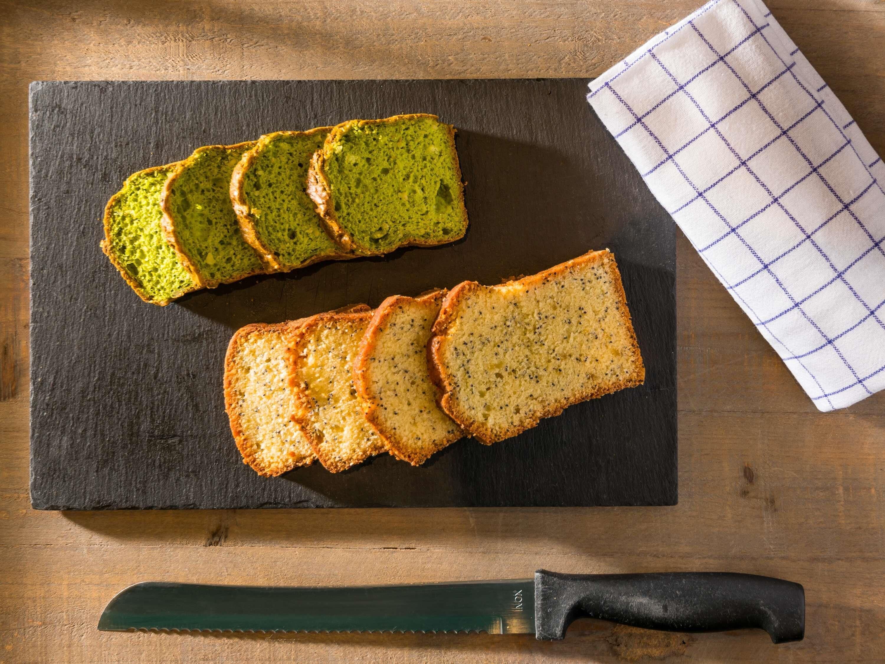 Fette di pane verde e normale su un tagliere in ardesia con un coltello e un tovagliolo a quadretti.