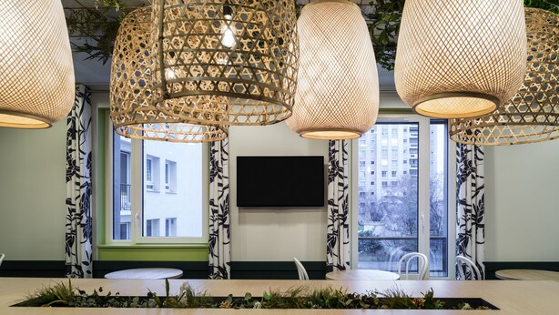 Un intérieur moderne avec un comptoir d’accueil, des rideaux à motifs et des lampes en rotin suspendues.