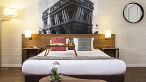 Une chambre d’hôtel avec un grand lit, deux tables de chevet, une petite table d’appoint, un miroir rond, une lampe fixée au mur et un objet décoratif sur la table de chevet.