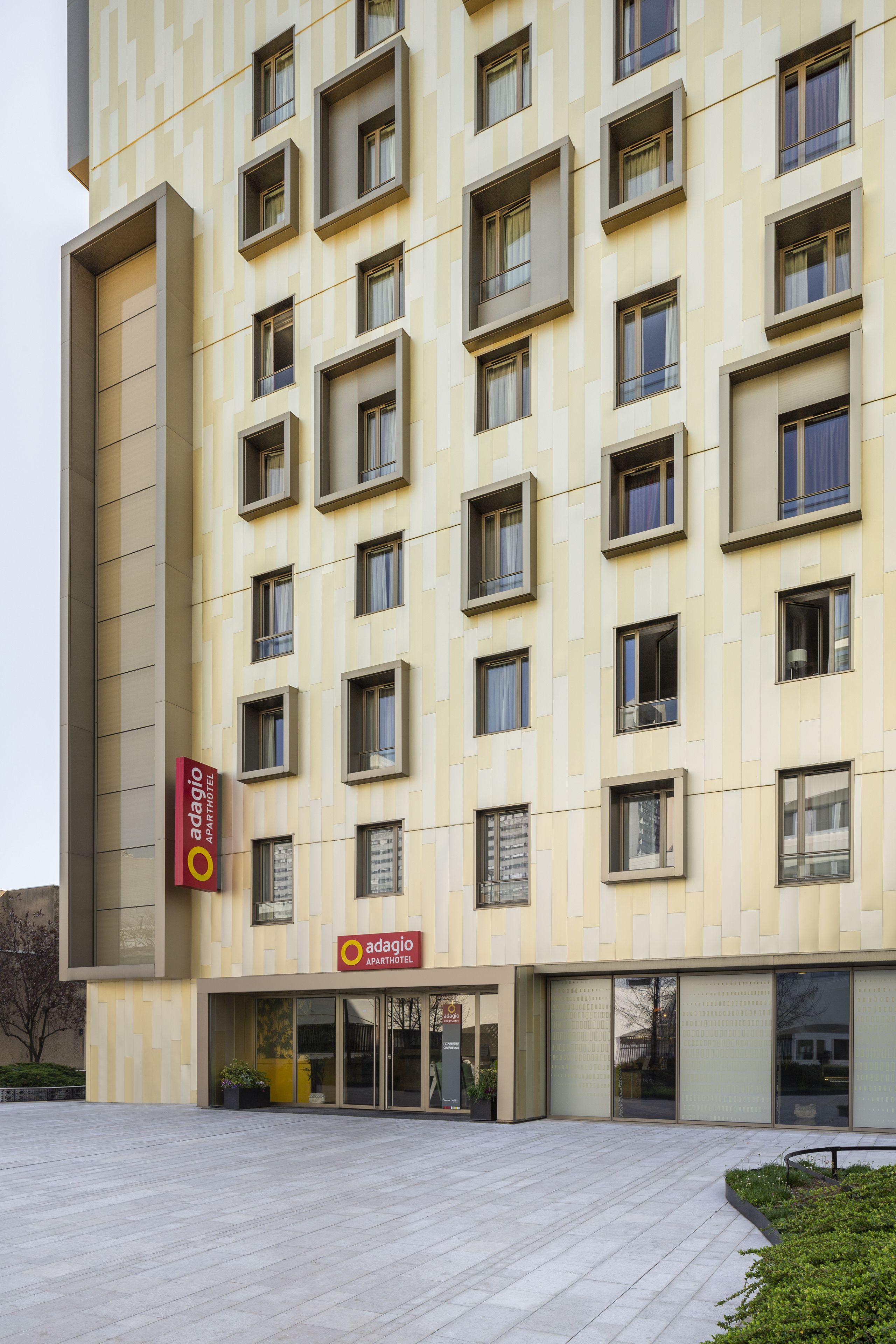 A modern building with a patterned facade, multiple windows, and a sign for 'Adagio Apartment Hotel'.