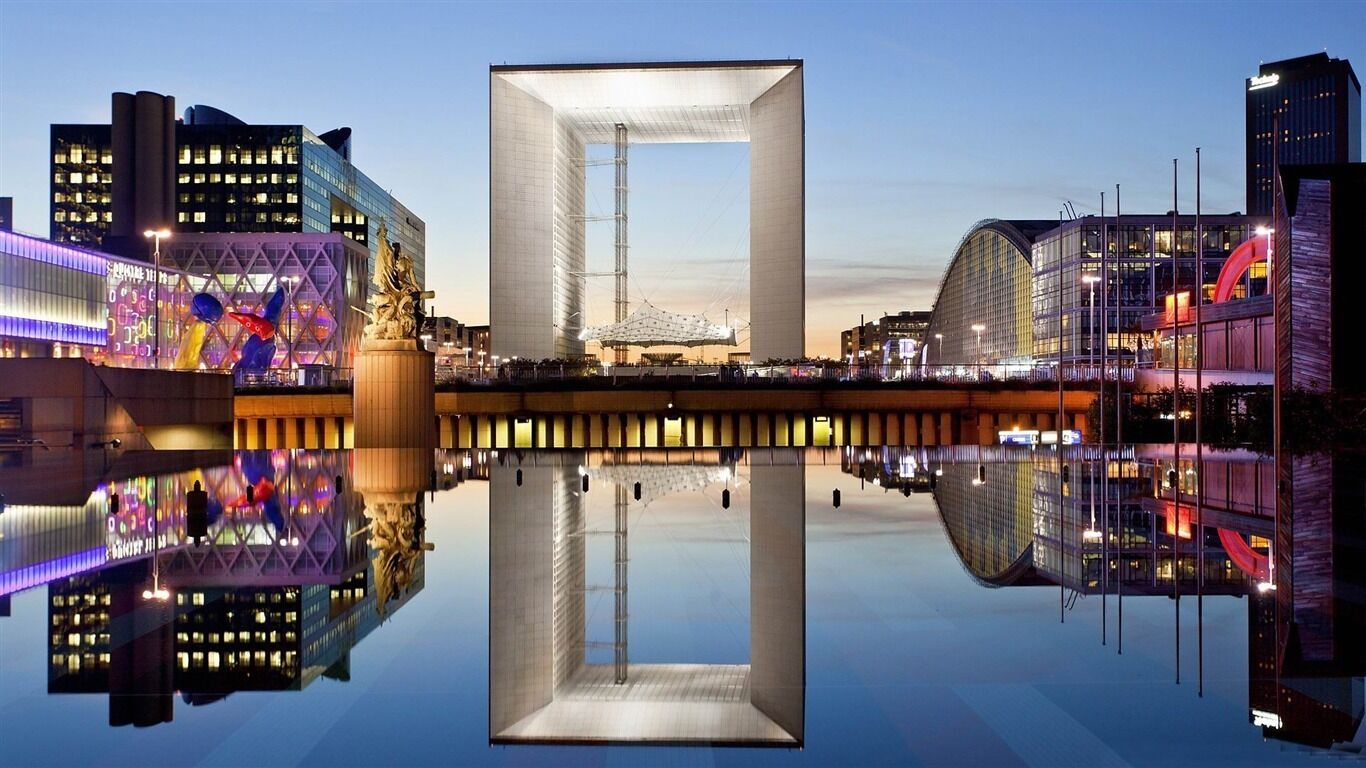 A modern building with a large central structure and a reflective pool in front.