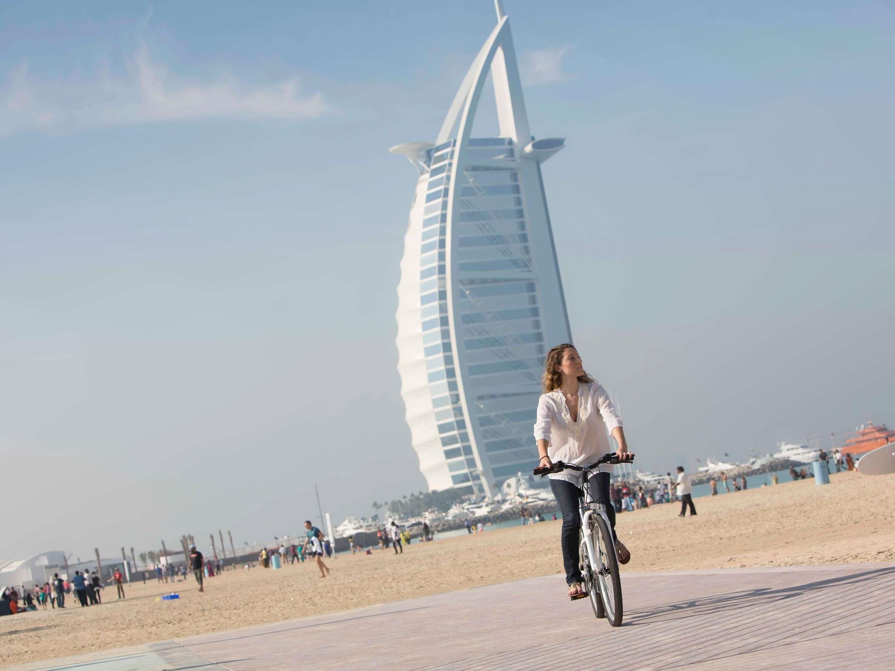 Una persona in bicicletta su un sentiero asfaltato, con un grande edificio moderno sullo sfondo.