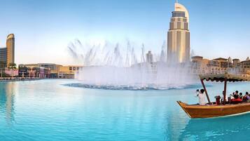 A waterfront view with a large fountain, a tall building, and a boat with people.