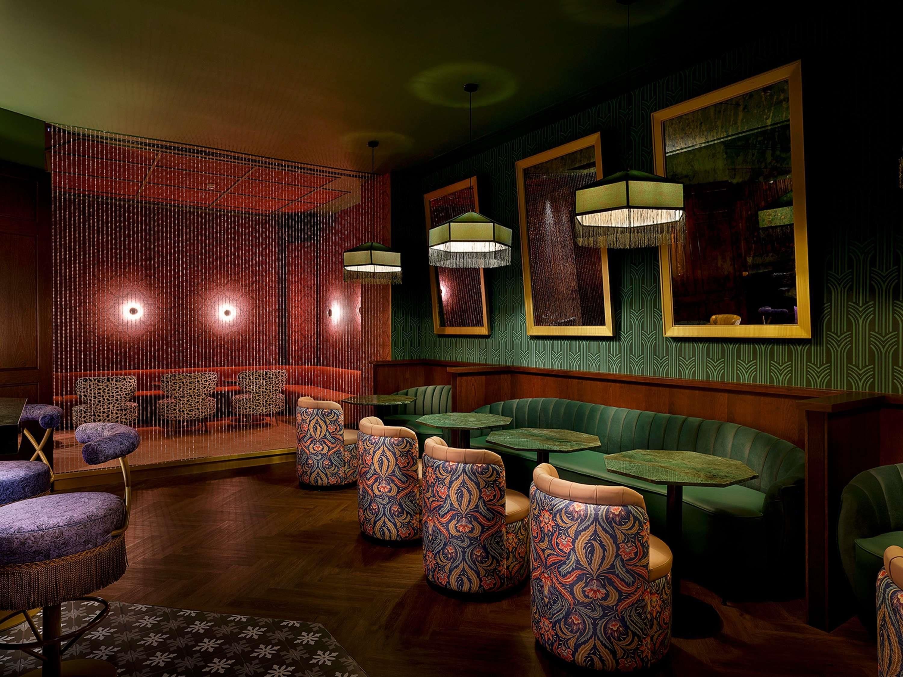 A dimly lit room with patterned seating, a green wall with framed artwork, and a red curtain backdrop.