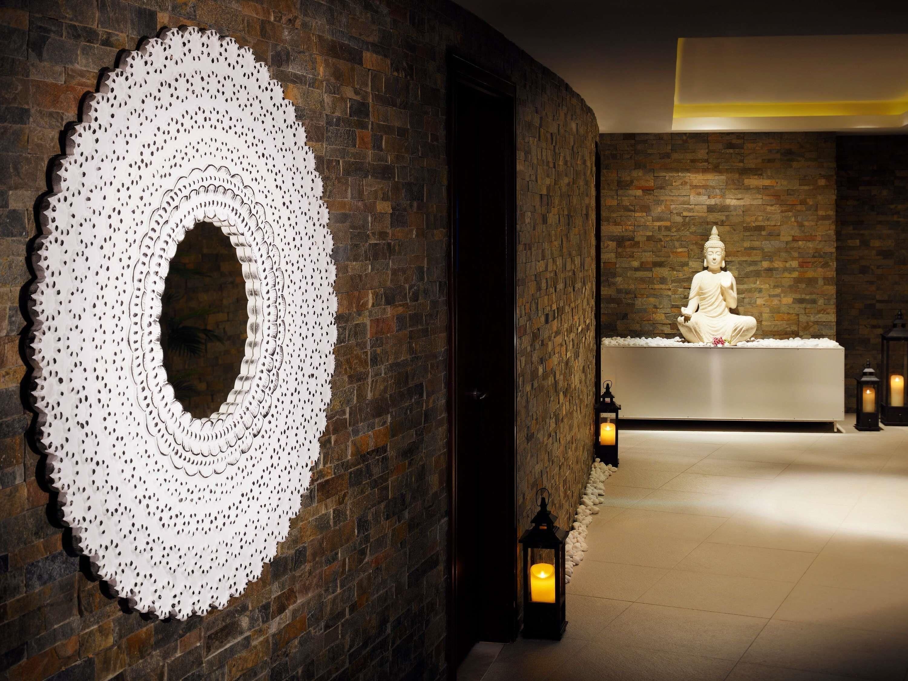 A serene spa area with a Buddha statue, a circular wall decoration, and a stone wall.