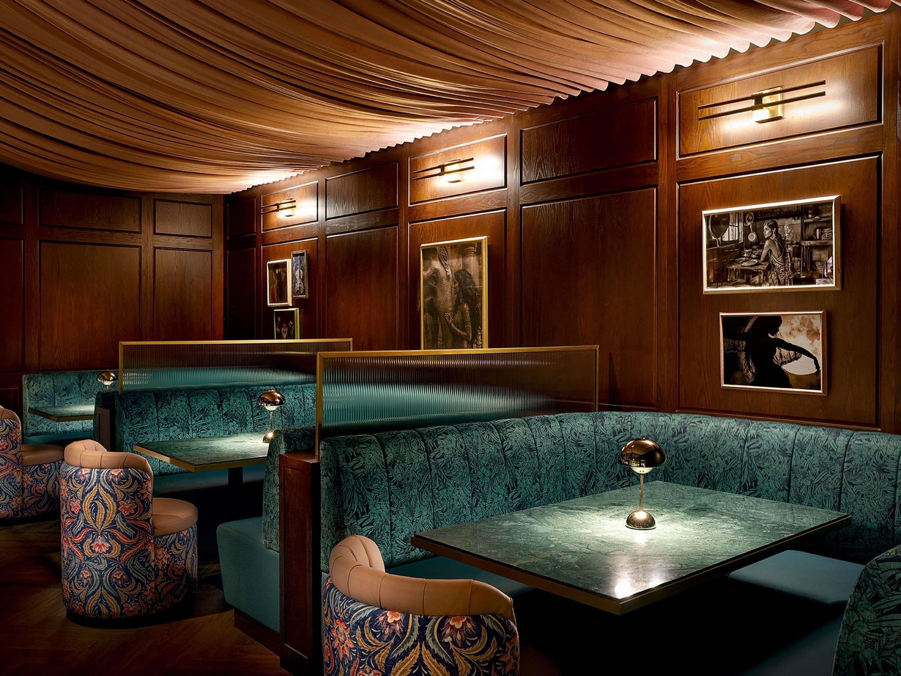 Ein Restaurant mit Holzwandverkleidung, grün gepolsterten Sitzecken und gerahmten Kunstwerken an den Wänden.