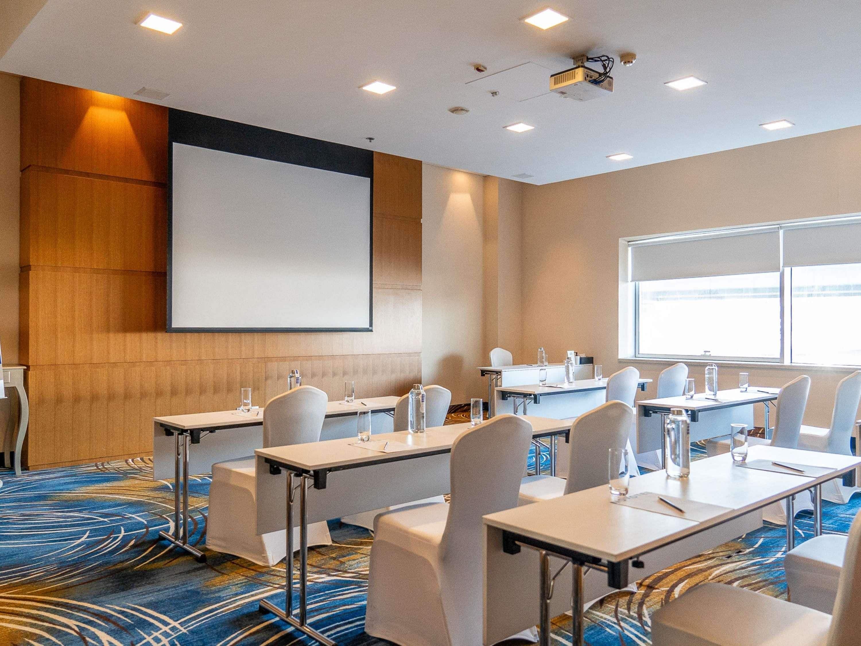 A conference room with tables, chairs, a projector screen, and a large window.