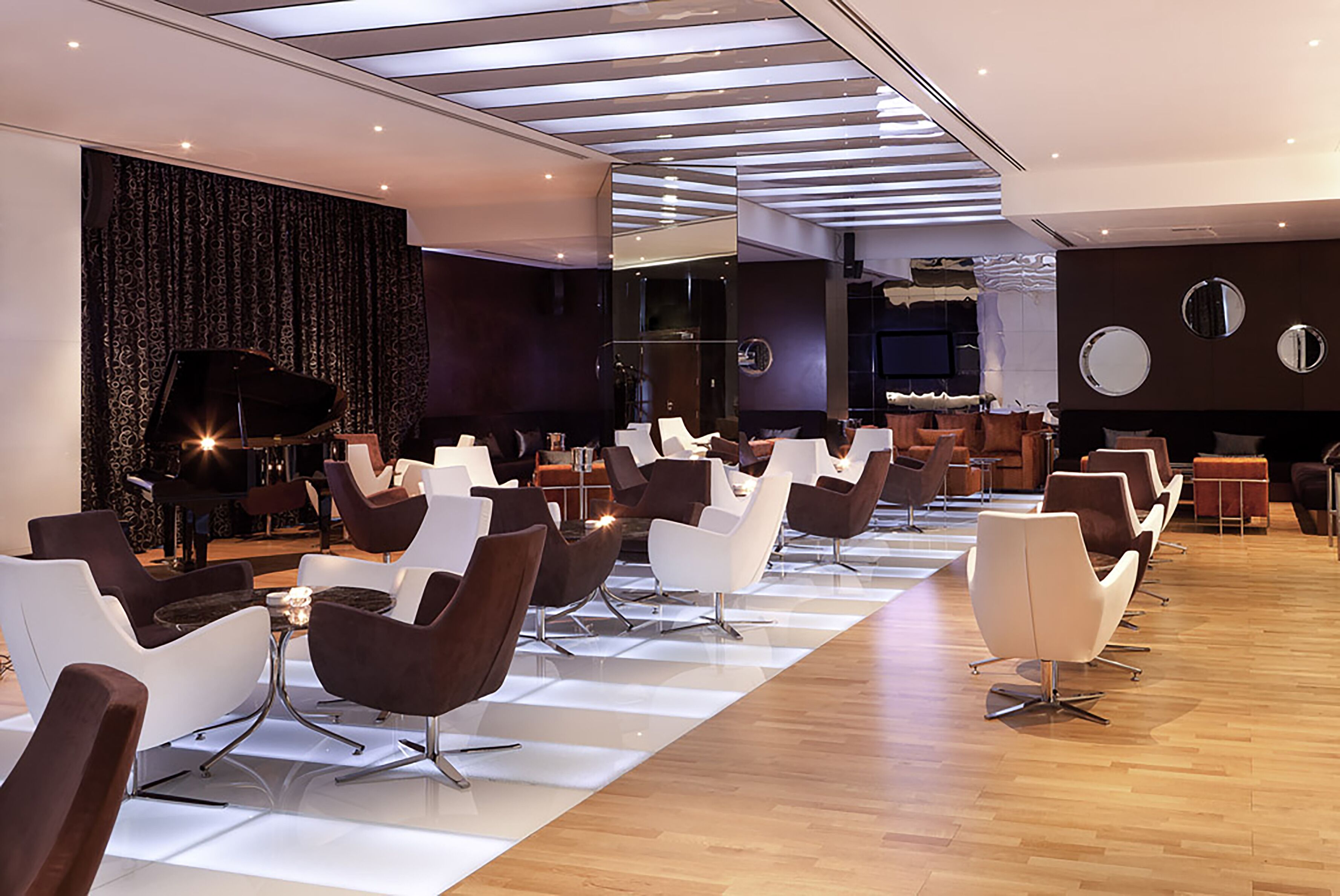 A modern lounge area with rows of contemporary chairs, a piano, and a large mirror wall.