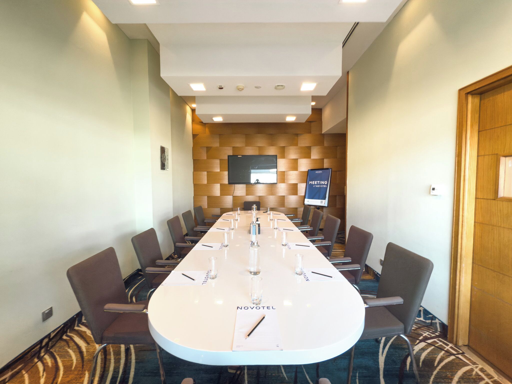 Une salle de réunion équipée d’une longue table, de chaises, d’un téléviseur et d’un panneau indiquant qu’il s’agit d’une salle de réunion.