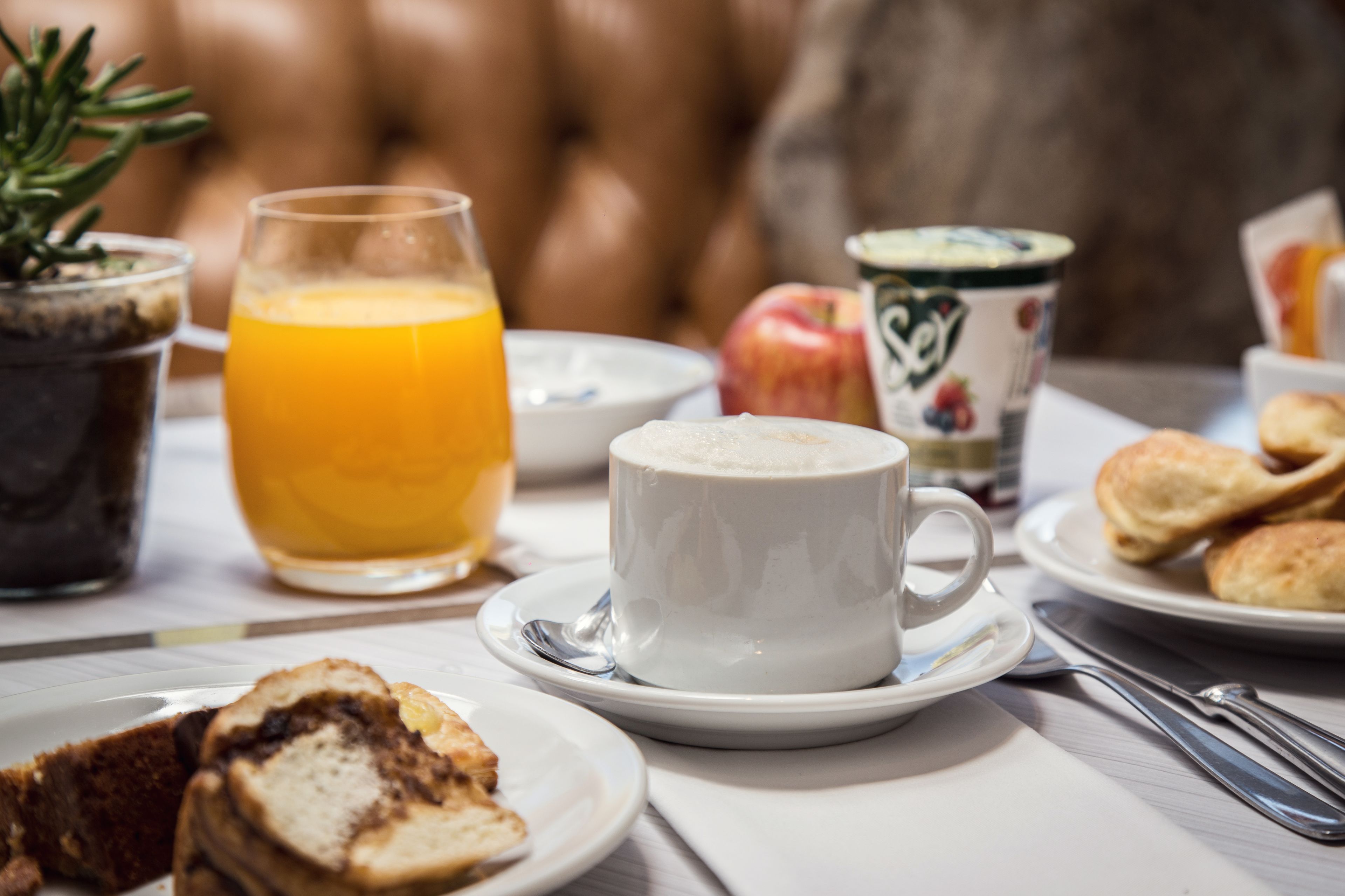 Desayuno servido con un vaso de jugo de naranja, una taza de café, un plato de pasteles y una planta en maceta.