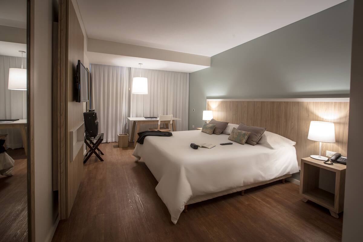 Quarto de hotel com cama grande, mesas de cabeceira, escrivaninha e uma cadeira.
