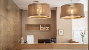 A reception desk with a wooden finish, two pendant lights, a 'biz' sign, a QR code, and a vase with flowers. - Brizo Neuquen (Neuquén)
