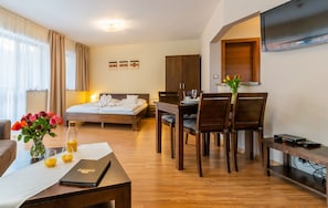 Quarto de hotel com cama, escrivaninha, mesa de jantar com cadeiras, televisão na parede e janela com cortinas.