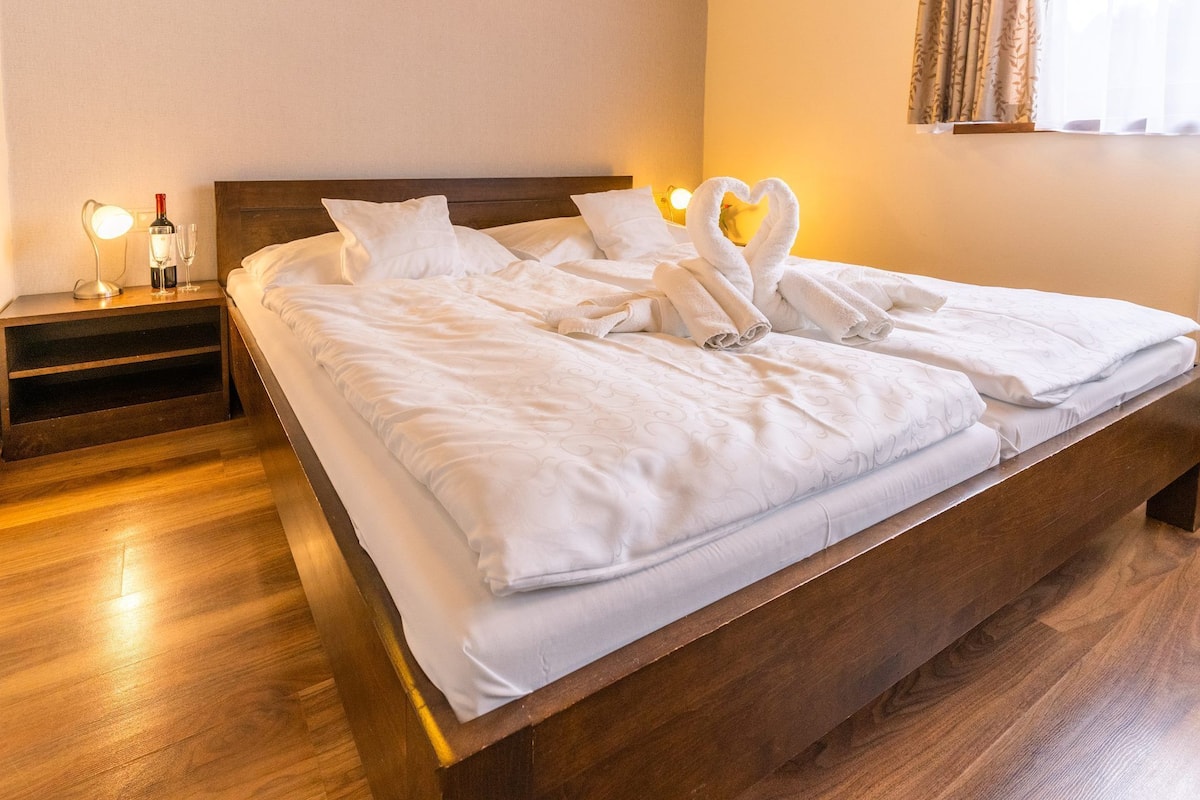 A neatly made bed with white linens, a wooden headboard, and a bedside table with a lamp and a bottle.