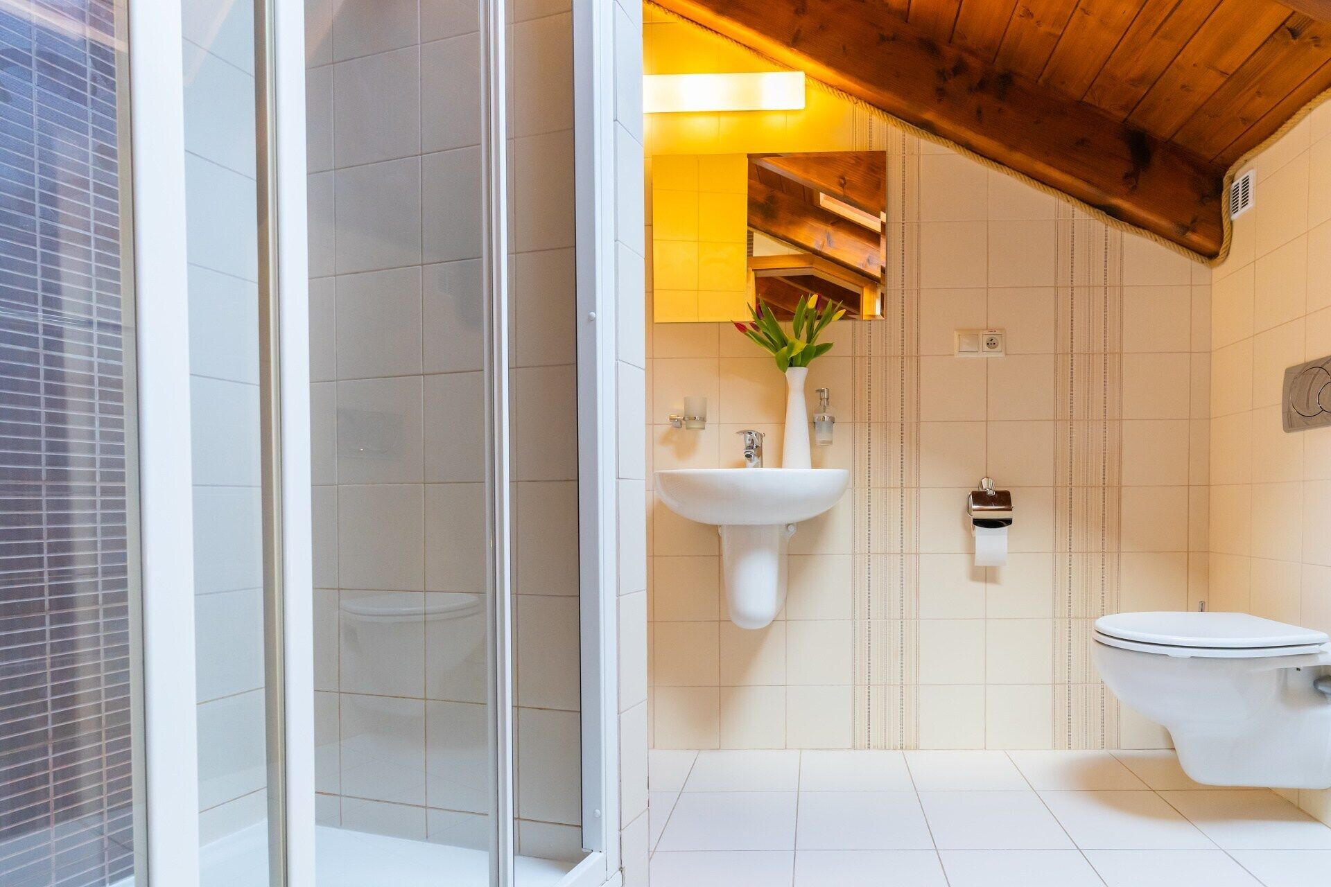 Une salle de bain moderne avec une douche à parois de verre, un lavabo blanc agrémenté d’un vase de fleurs et des toilettes.