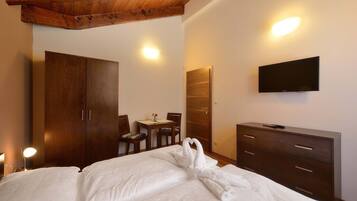 Une chambre d’hôtel avec un plafond en bois, un lit recouvert de draps blancs, une commode en bois, un téléviseur fixé au mur et un coin repas avec une table et des chaises.